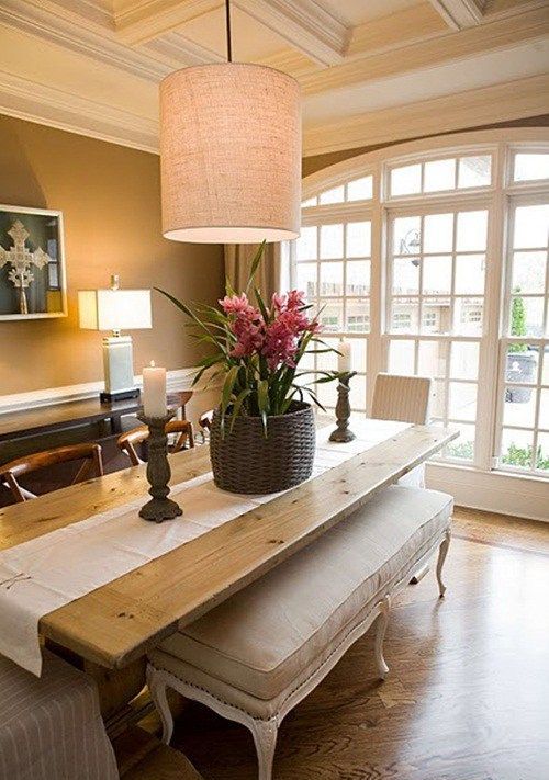 a welcoming taupe dining room with a dark console table, a stained table and neutral benches, some lamps and a basket with blooms