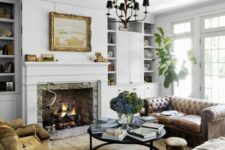 a white vintage living room with a vintage stone hearth, built-in bookcases, a leather sofa, rust chairs, a round coffee table