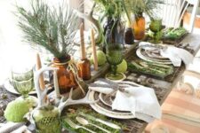 a woodsy Thanksgiving tablescape with evergreens, pea balls, moss, patterned plates and stick placemats