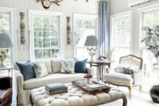 an airy vintage living room with chic vintage furniture, a large ottoman, chic chandeliers, blue curtains and greenery