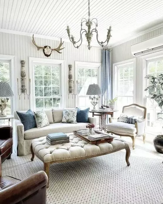 an airy vintage living room with chic vintage furniture, a large ottoman, chic chandeliers, blue curtains and greenery