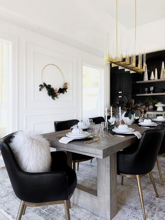 an elegant black and white dining room with a black accent wall and cabinets, a stained table, black chairs and a gilded chandelier