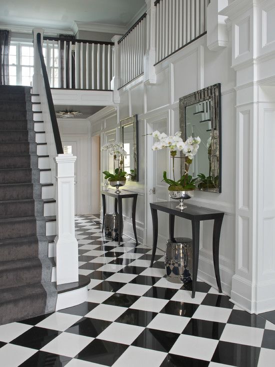 an elegant black and white foyer with checked tiles, black console tables, mirrors in chic frames and potted orchids