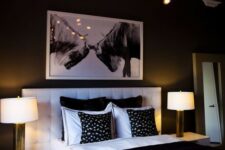 an elegant contemporary bedroom with a white upholstered bed, white nightstands, a chic chandelier and an artwork