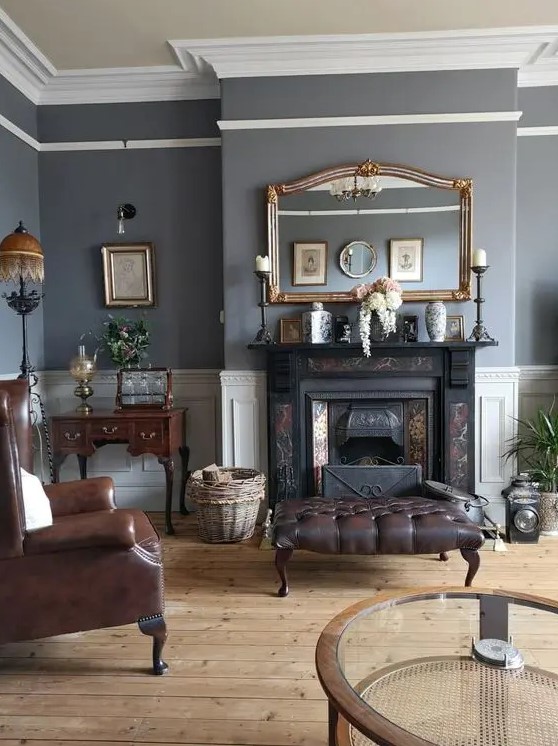an elegant vintage living room with grey walls, a black fireplace, brown leather chairs and ottomans, a mini desk and artwork