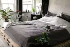 an industrial bedroom with shabby chic walls, a pallet bed with black and white bedding, a bike and a pendant lamp