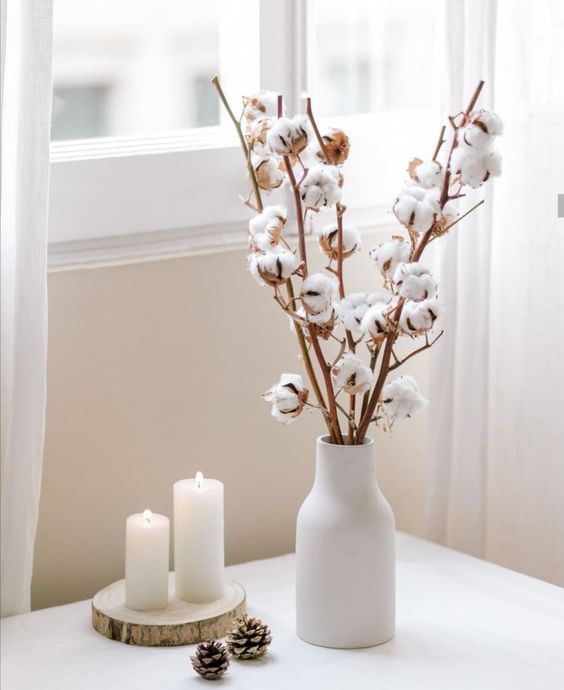 minimalist Thanksgiving decor with a white vase with cotton branches, pinecones and pillar candles on a tree slice