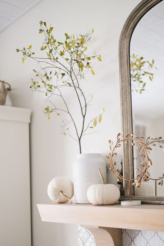 minimalist Thanksgiving mantel decor with white pumpkins, a white vase with a yellow branch and a mini gold wreath on a stand