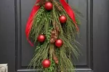 02 a bold Christmas evergreen posie with pinecones and red ornaments plus a large red bow on top is a cool front door decoration