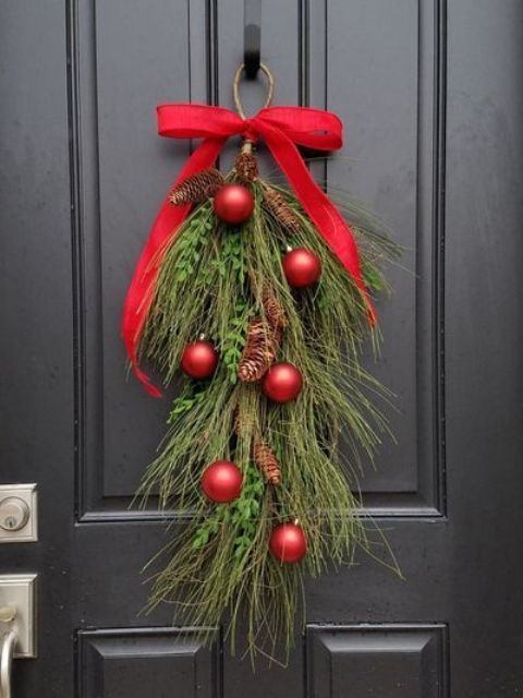 a bold Christmas evergreen posie with pinecones and red ornaments plus a large red bow on top is a cool front door decoration