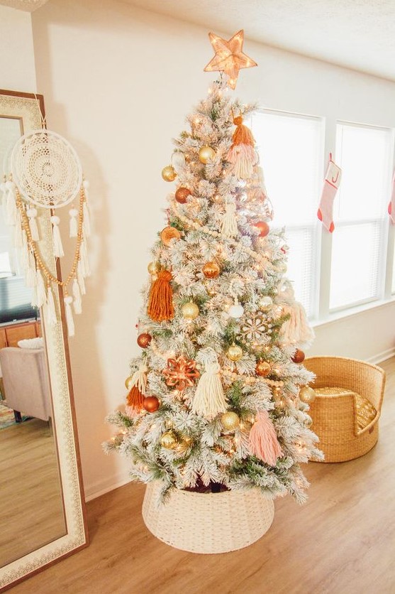 a lovely flocked Christmas tree with pastel boho decor, orange, gold and blush ornaments, beadsm large tassels and lights