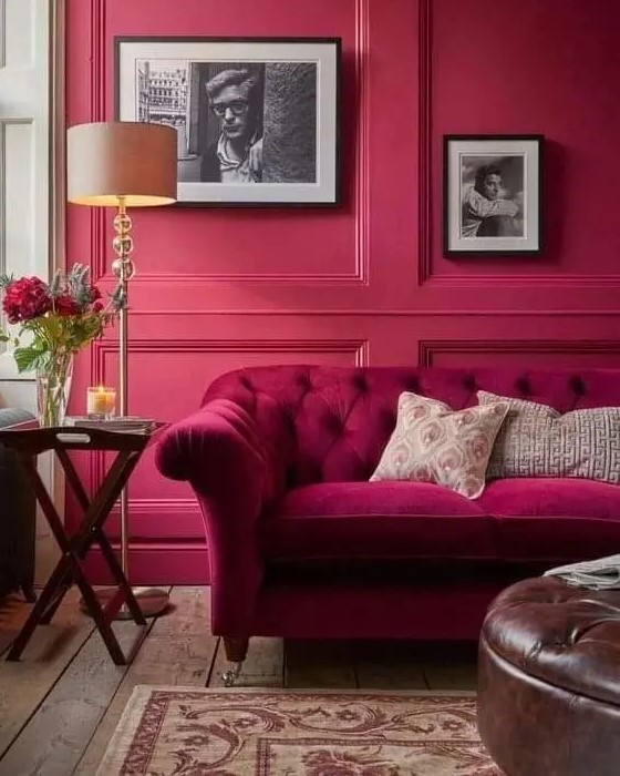 a magenta living room with a matching sofa, a leather ottoman, some artworks and a side table plus a floor lamp
