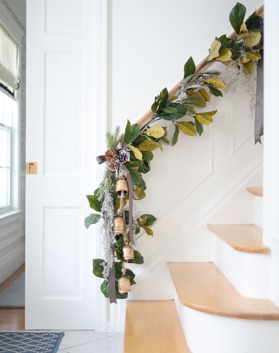 a beautiful leafy Christmas garland with snowy pinecones and bells is a stylish and out of the box idea of Christmas decor