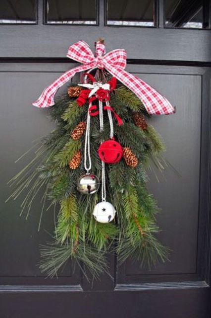 a bold Christmas swag with evergreens, pinecones, white, red and silver bells and a red and white plaid bow on top