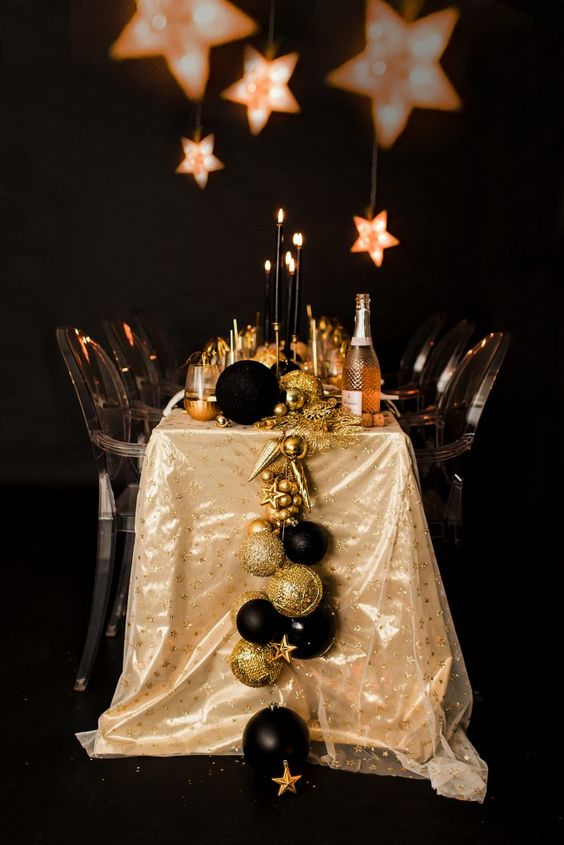 a black and gold NYE tablescape with a large ornament and star runner, black candles and lots of black glitter