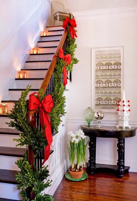 a boxwood garland with red bows and lanterns on the stairs are great and very elegant staircase decor for Christmas