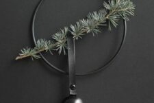 04 a minimalist Christmas wreath in black with an evergreen branch and a black bell hanging on a black leather loop