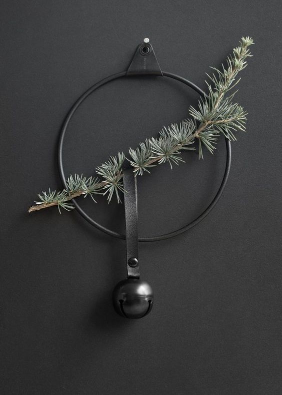 a minimalist Christmas wreath in black with an evergreen branch and a black bell hanging on a black leather loop