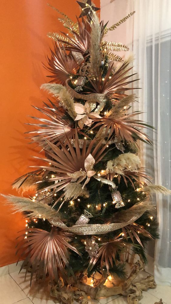 a Christmas tree with fronds, pampas grass, fabric blooms and lights plus gilded leaves is a cool idea for a tropical holiday space