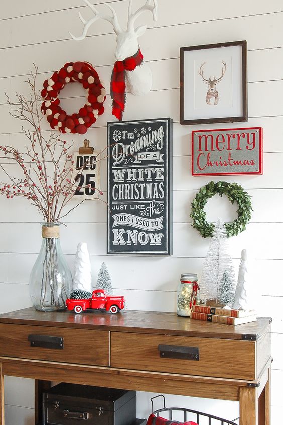 a cool Christmas entryway gallery wall with several signs, a calendar, artworks, a greenery wreath and a fake deer head in a scarf