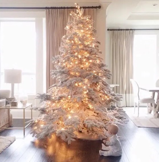 a large flocked Christmas tree decorated with only lights is a fantastic idea for winter wonderland feel in the space