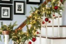 07 a fir Christmas garland with lights and red ornaments hanging is a beautiful idea for Christmas banister decor