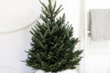 07 a minimal Scandinavian Christmas tree decorated with only lights, with a basket and faux fur is a chic and easy to realize idea