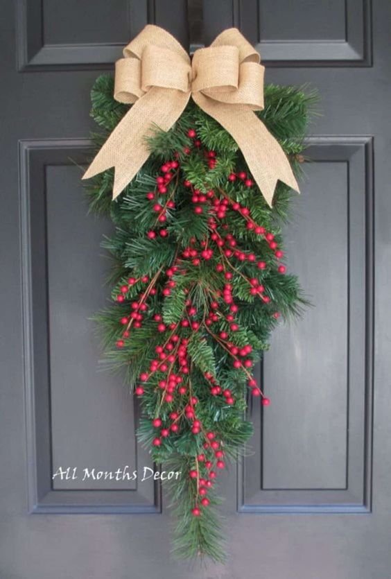 a simple and cute evergreen poise with red berries and a burlap bow on top is a lovely idea for a Christmas front door