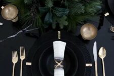 08 a black table with black plates and cahrgers, lush evergreens and gold cutlery for a moody tablescape