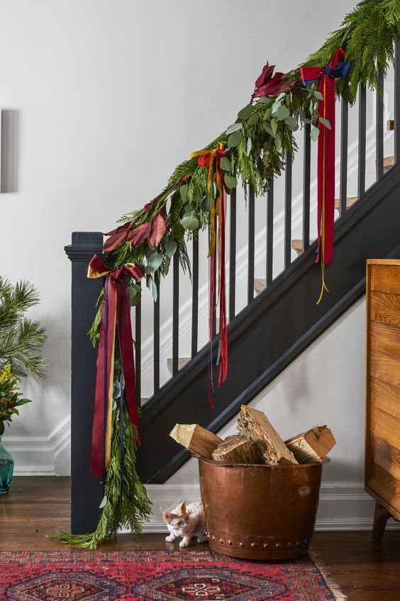 a greenery garland with leaves and bold red ribbon bows is a bold and cool decor idea for Christmas