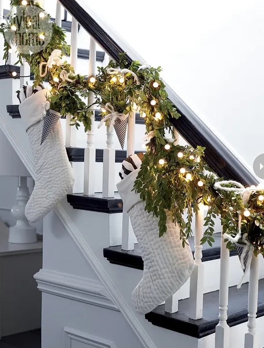a greenery garland with lights, paper cones, large white stockings is a lovely piece to decorate railing for Christmas