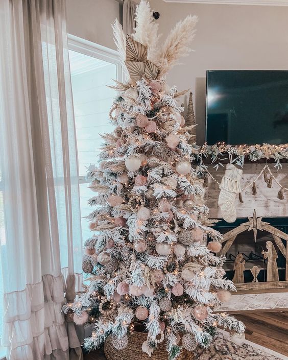 a neutral boho Christmas tree with creamy and pink ornaments, wooden beads, pampas grass and fronds and lights