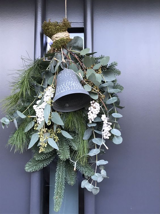 an evergreen Christmas swag with foliage, wihte berries, moss and a large bell is a lovely front door decor idea