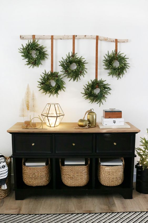a branch with evergreen and pinecones wreaths hanging down is a lovely wall decoration for the holidays