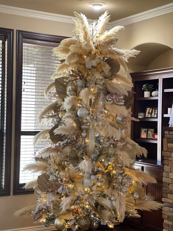 a pampas grass Christmas tree decorated with large metallic ornaments, lights and fronds and topped with some branches