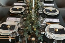 12 a dreamy NYE tablescape in black, with black linens, white porcelain, a greenery runner with LED lights, tall and thin candles