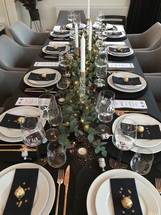 a dreamy NYE tablescape in black, with black linens, white porcelain, a greenery runner with LED lights, tall and thin candles