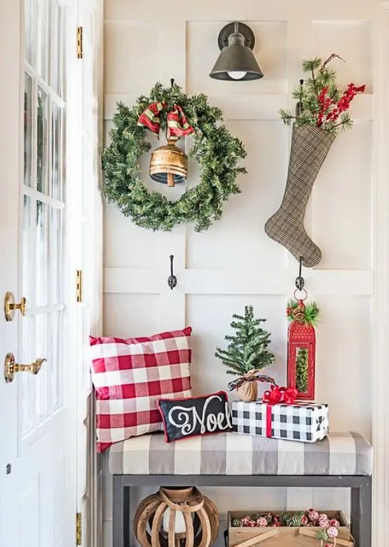 a large greenery wreath with a bell and a plaid stocking with evergreens and berries hanging on hooks