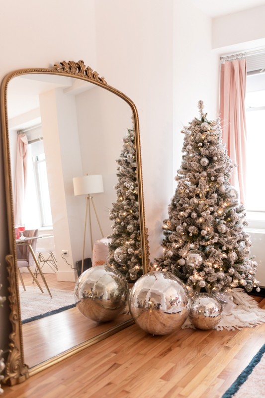 a silver Christmas tree decorated with matching silver disco balls and ornaments and with disco balls by its side