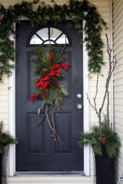 an evergreen swag with branches, pinecones and red blooms plus an evergreen garland with lights over the door for Christmas