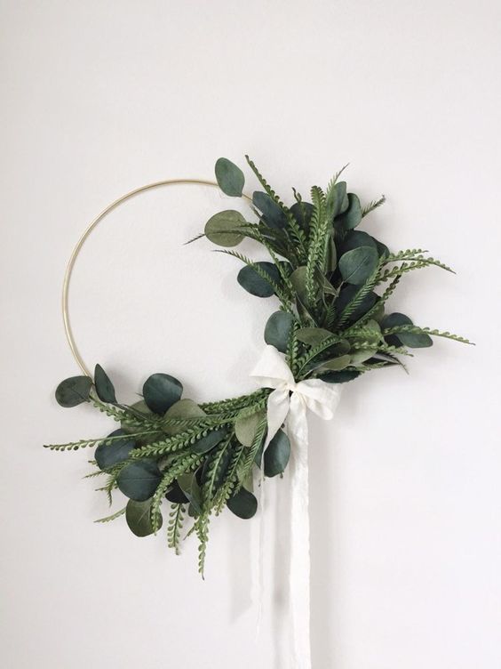 a cool modern Christmas wreath with several types of greenery attached only on one side, with a white ribbon bow