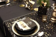 14 a glam black and gold NYE party table with star printed placemats, black plates and gold chargers, gold candles and stars