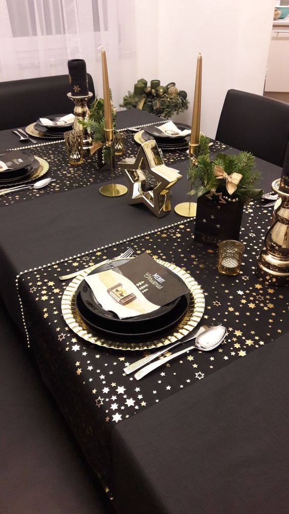a glam black and gold NYE party table with star printed placemats, black plates and gold chargers, gold candles and stars