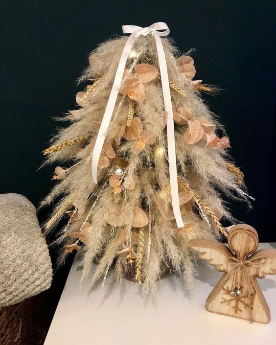 a small tabletop pampas grass Christmas tree decorated with wheat and some leaves plus lights and a bow for a boho space