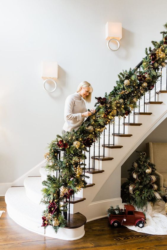 a sophisticated evergreen banister garland with gold ornaments, lights, soem faux blooms and metallic ornaments