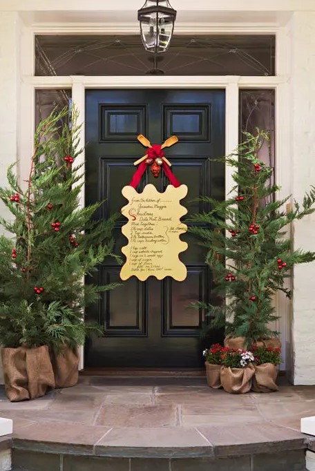 a Christmas front door with an artwork with song lyrics, Christmas trees with red ornaments and blooms in burlap