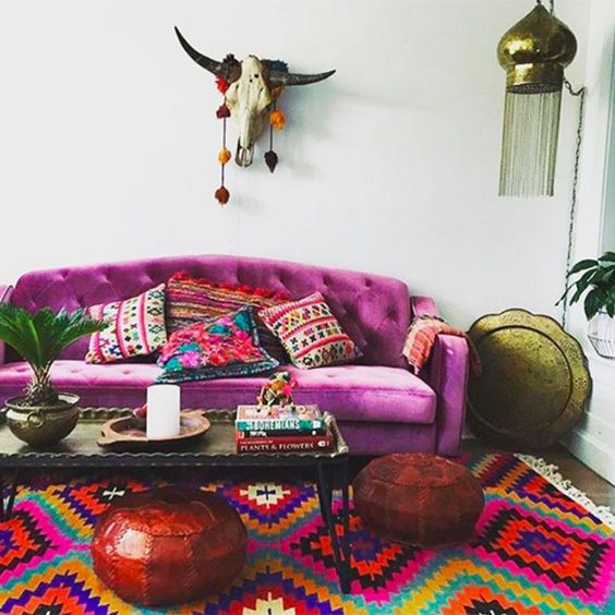 a bright boho living room with a fuchsia sofa and bold pillows, a bright printed rug, a coffee table, leather poufs and some boho decor