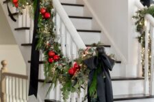 16 a stylish evergreen and leaf garland with red ornaments, lights and black bows is a great decoration for a banister