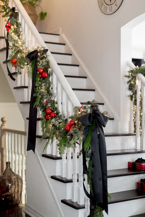 a stylish evergreen and leaf garland with red ornaments, lights and black bows is a great decoration for a banister