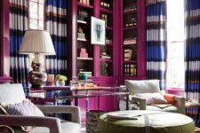 17 a bright home library with magenta bookcases, striped curtains, a tiered table, upholstered chairs and a large ottoman